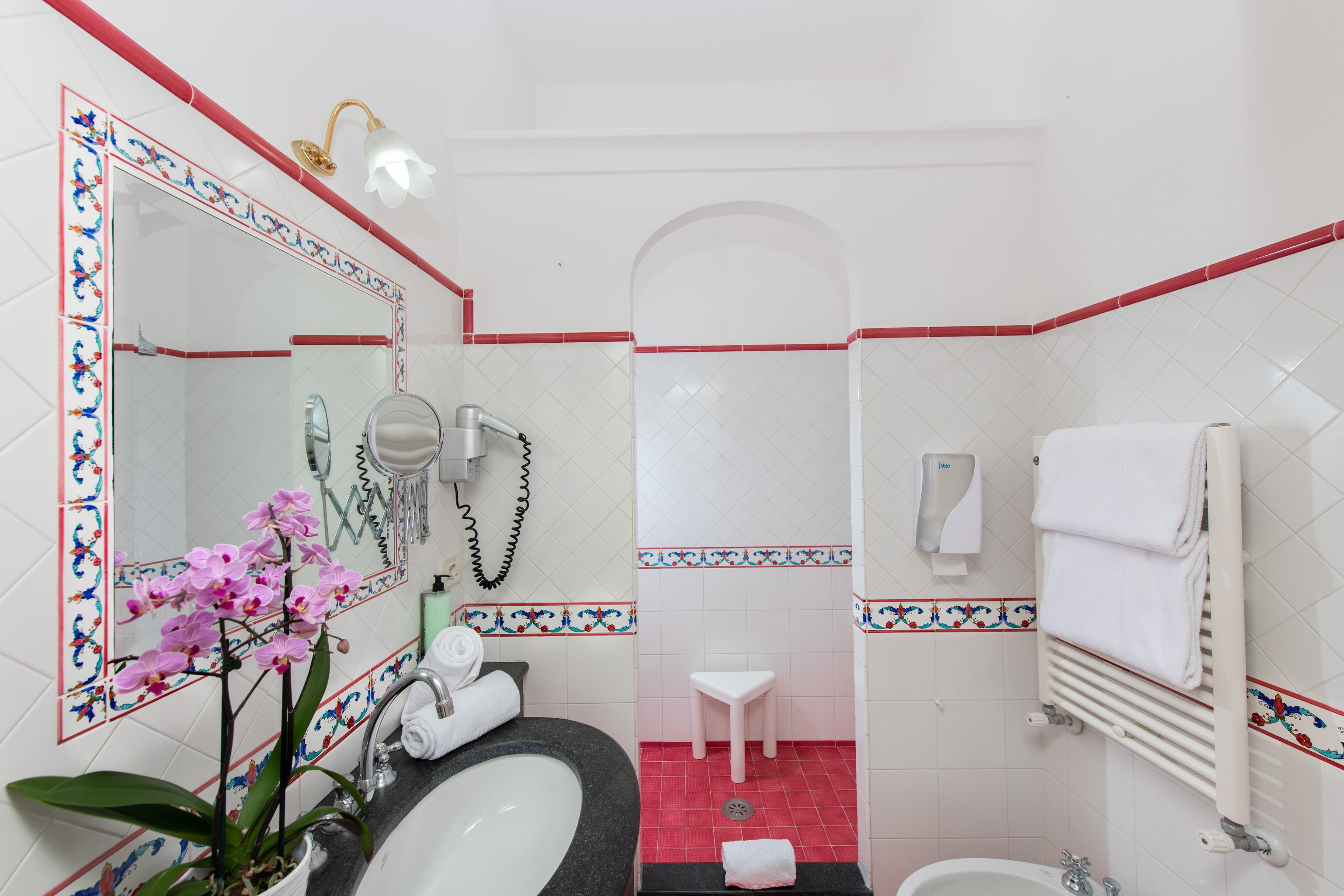 A bathroom with a large mirror, a sink, a toilet, a small white stool, and a towel rack.