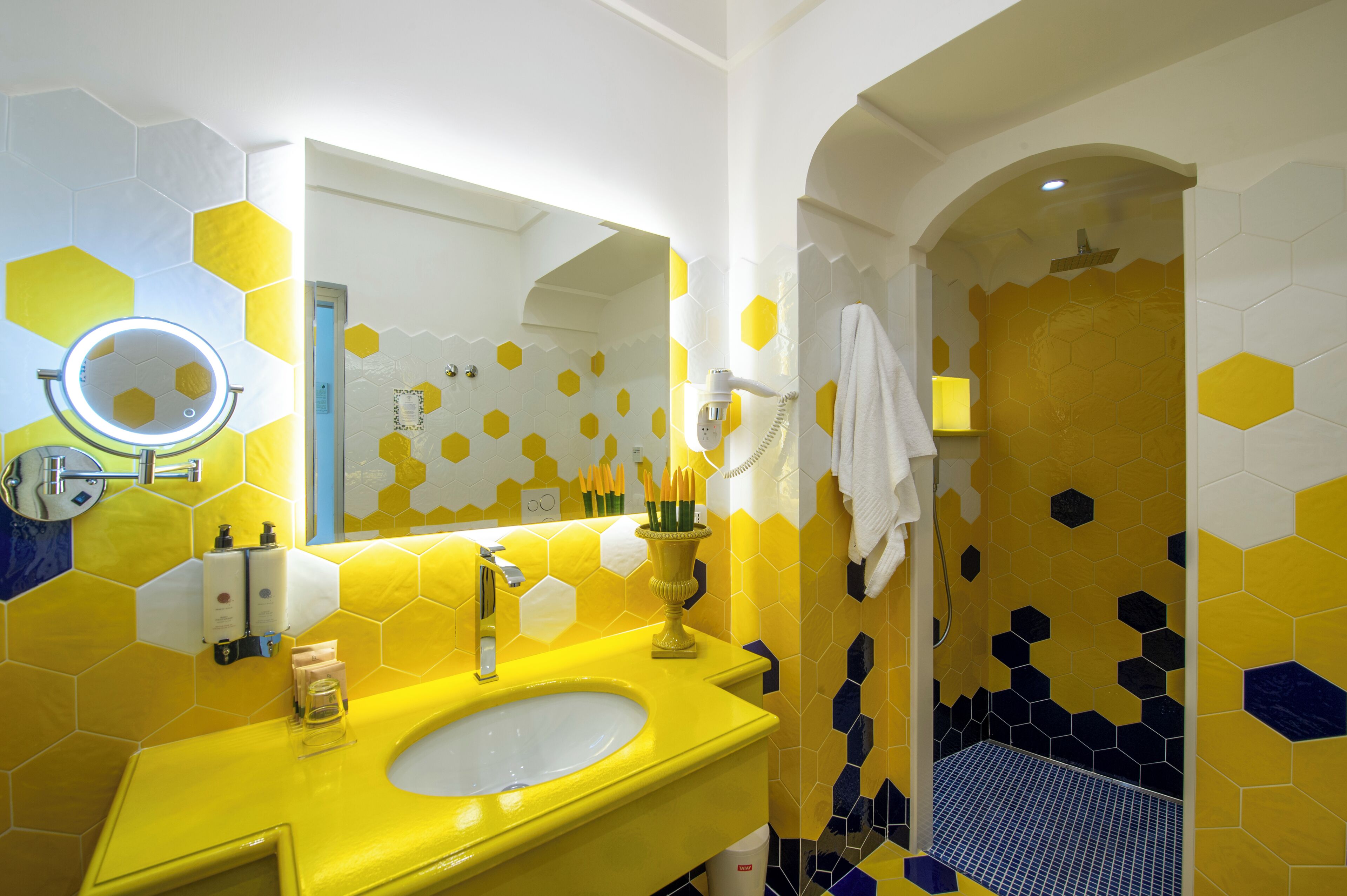 A bathroom with a yellow sink, a mirror, and a shower area with hexagonal tiles.
