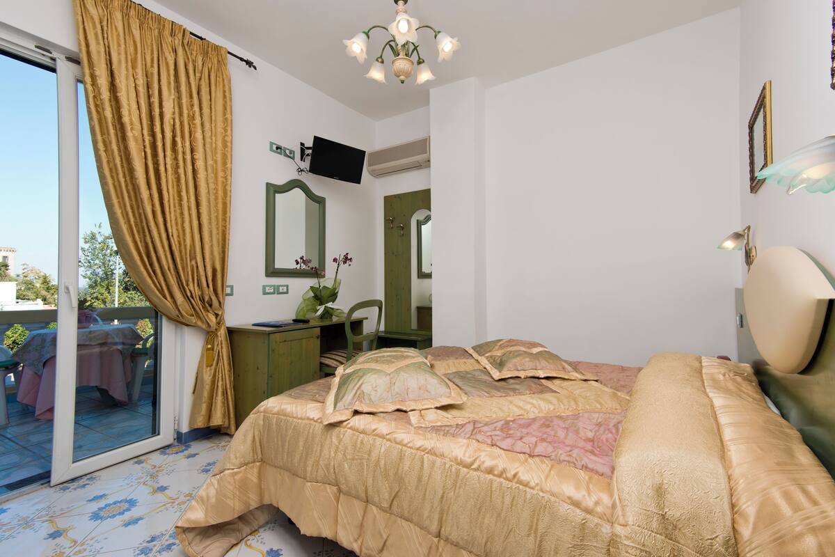 Un dormitorio con una cama grande, un escritorio, una silla, un televisor y un ventanal corredero que da a un espacio exterior.
