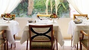 A dining area with tables set for two, white tablecloths, and a view of greenery through a window. - Adua & Regina di Saba (Montecatini Terme)