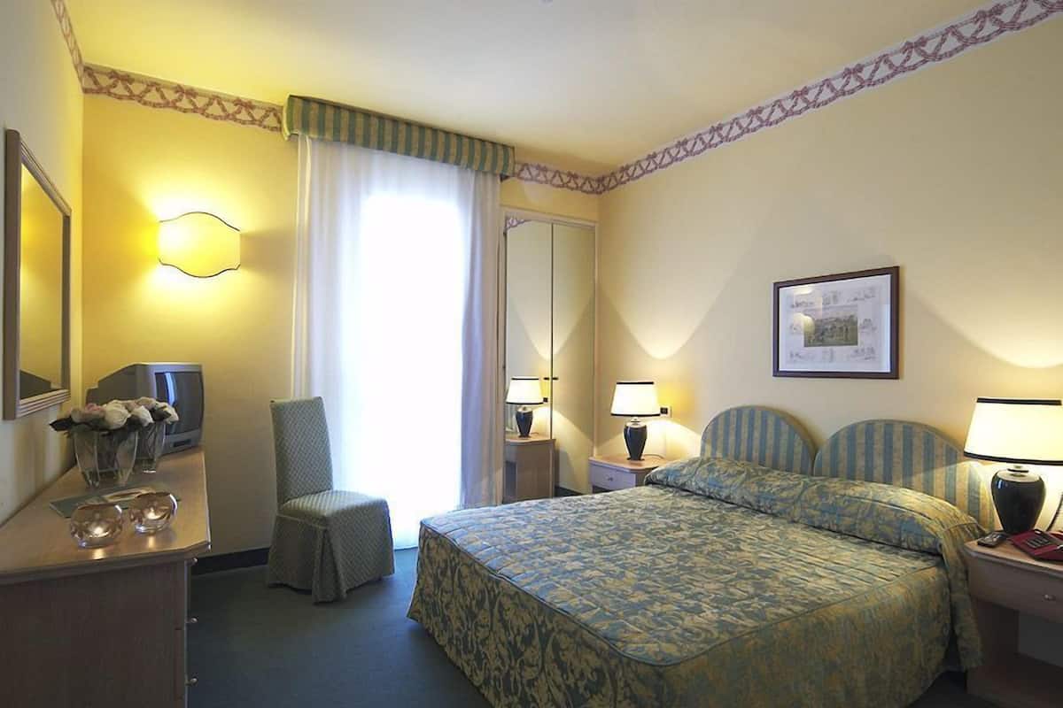 A hotel room with a bed, a chair, a desk with a lamp, a television, and a mirror.