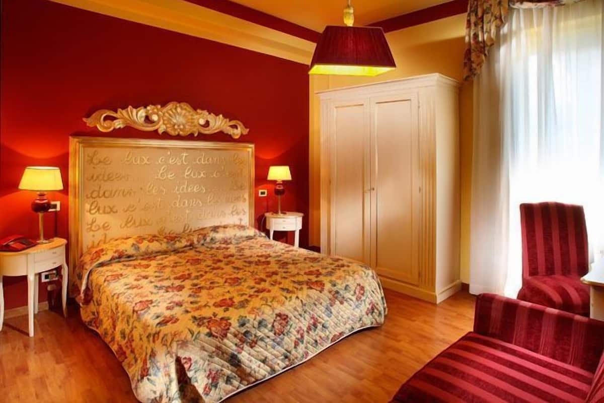 A bedroom with a floral bedspread, a white wardrobe, a red armchair, and two bedside lamps.
