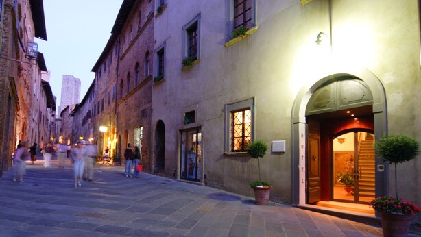 A historic street with a hotel entrance featuring an arched doorway and potted plants. - Hotel L' Antico Pozzo San Gimignano (San Gimignano)