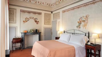 Un dormitorio con cama, mesitas de noche, chimenea y detalles decorativos en el techo.