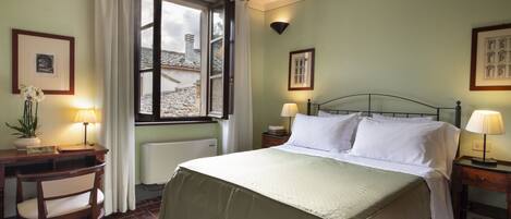 A bedroom with a bed, a desk, a chair, a window with curtains, and a radiator.