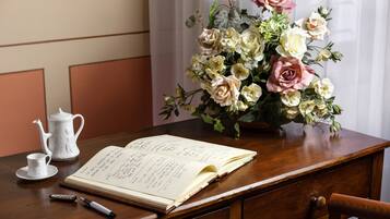 Un escritorio de madera con un cuaderno, un bolígrafo, una tetera y un arreglo floral.