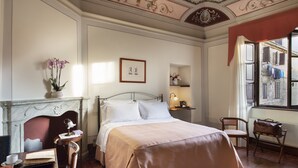 A bedroom with a bed, a desk with a chair, a fireplace, and a window with a view of buildings. - Hotel L' Antico Pozzo San Gimignano (San Gimignano)