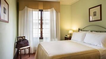 A hotel room with a bed, a chair, a nightstand, and a window with curtains.