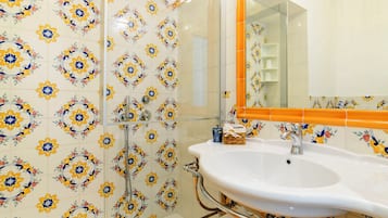 Un bagno con un lavandino bianco, box doccia in vetro e uno specchio con cornice arancione.