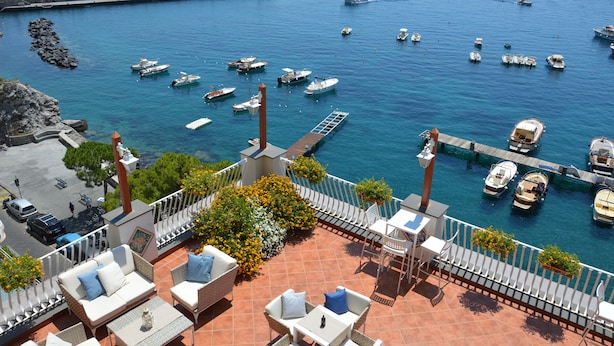 Terraza con mobiliario exterior que ofrece vistas a un puerto deportivo con varias embarcaciones.