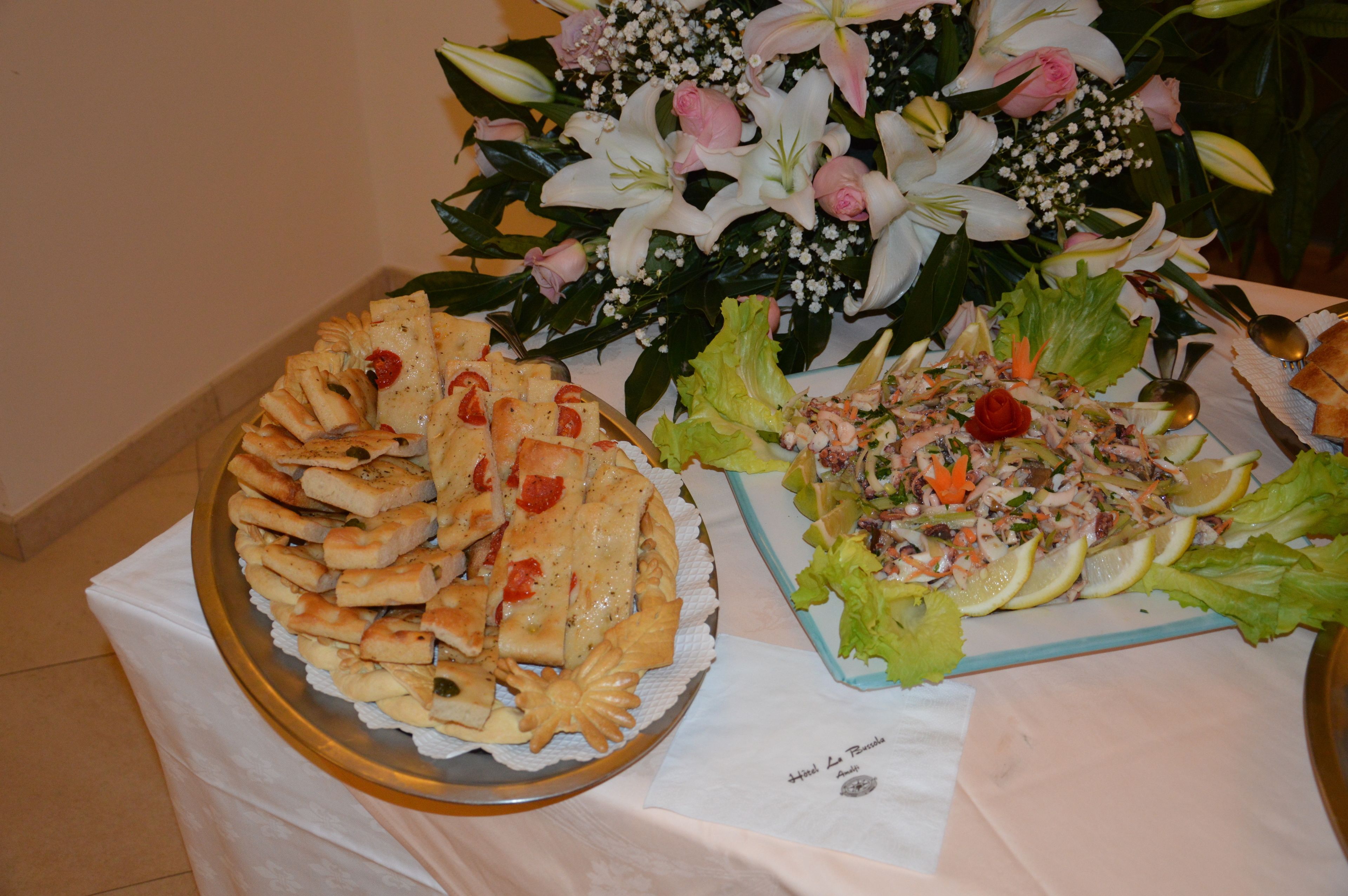 Una mesa de buffet con diversos platos, incluyendo una bandeja de panecillos y una ensalada con rodajas de limón.