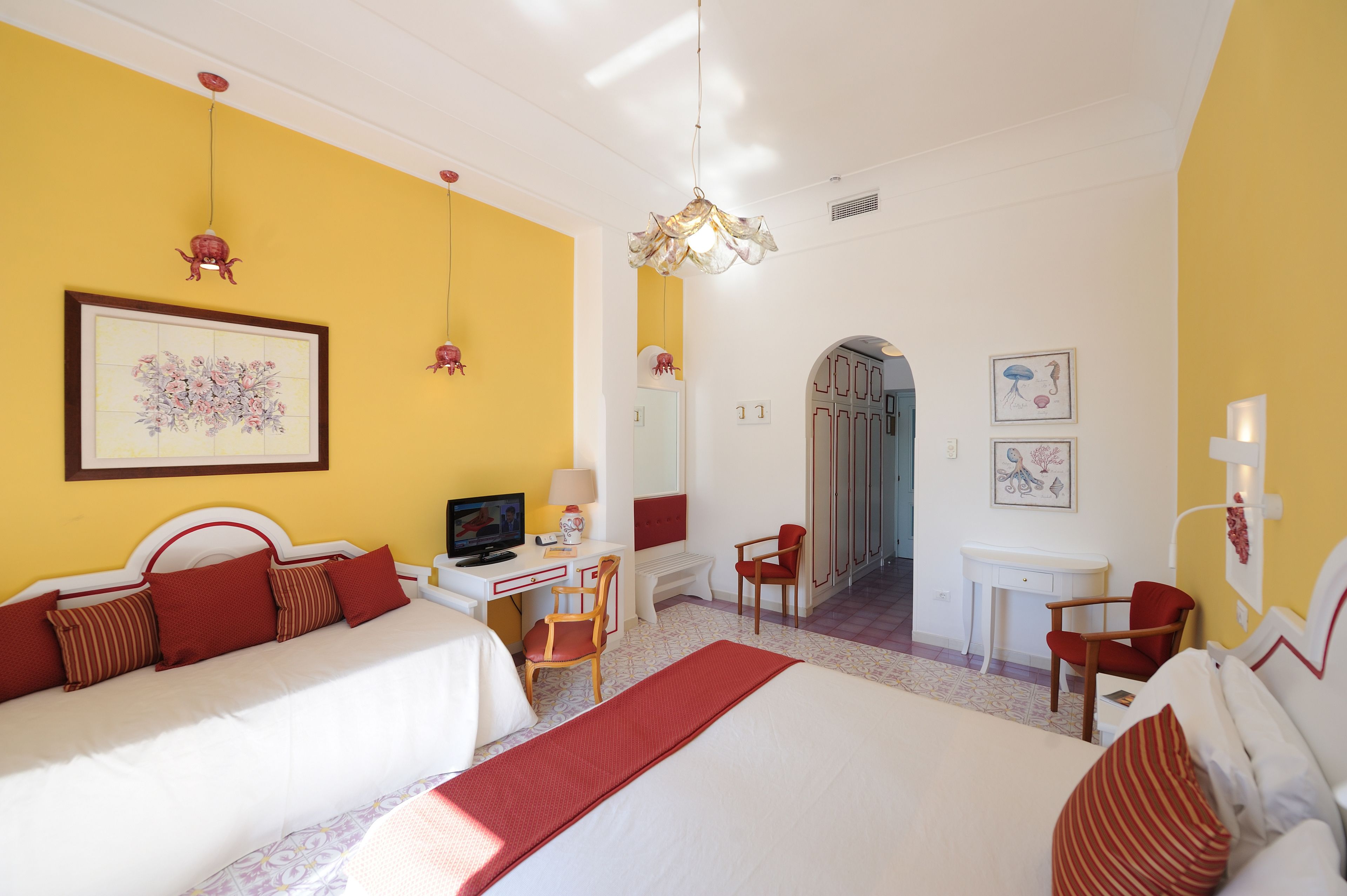 A hotel room with two beds, a desk, a chair, a TV, and artwork on the walls.