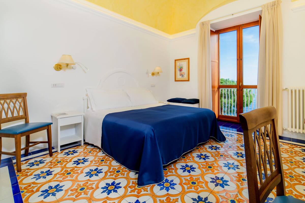 A bedroom with a bed, a chair, a nightstand, and a window with a view.