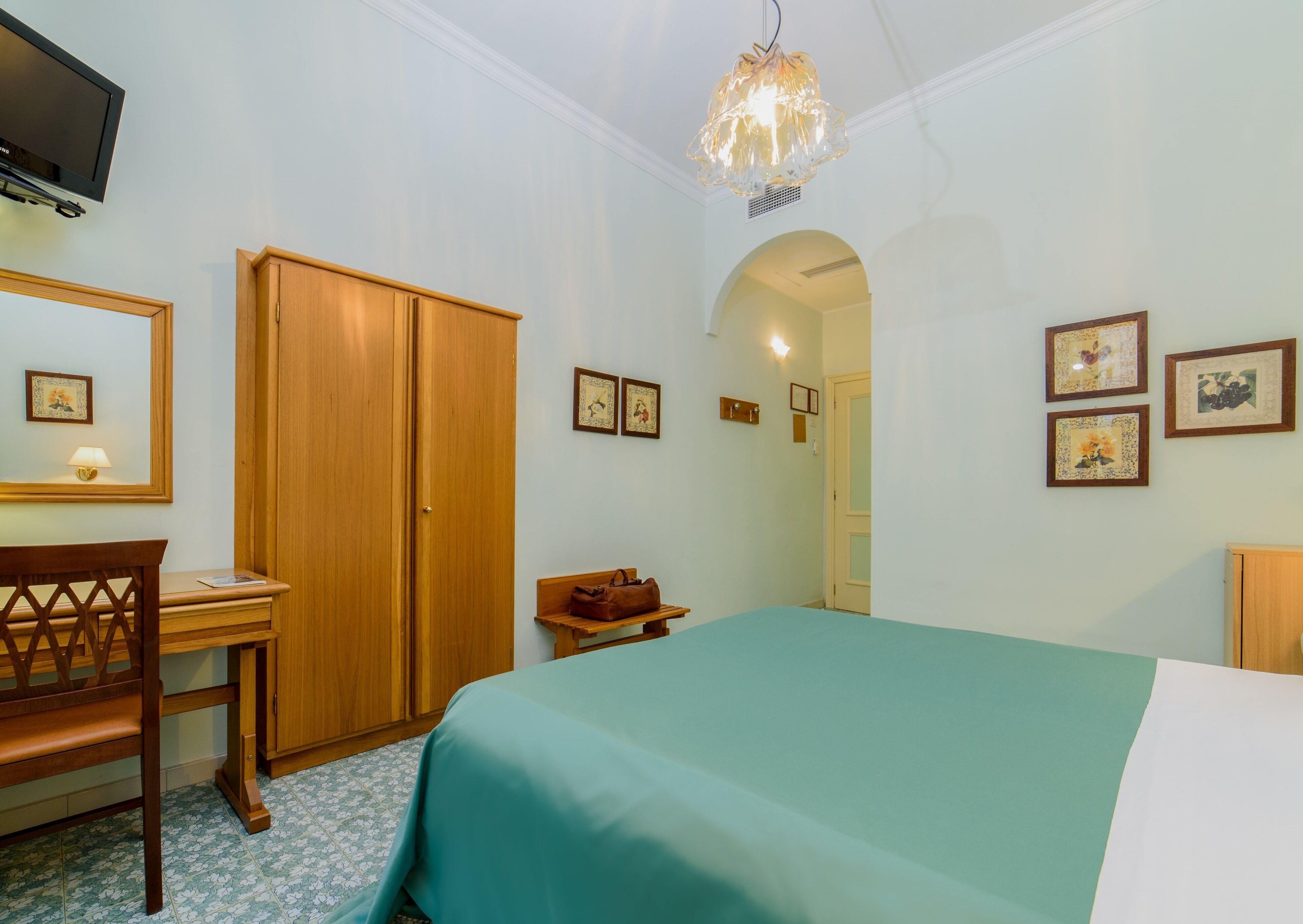 A bedroom with a bed, a desk, a chair, a wardrobe, and a television.