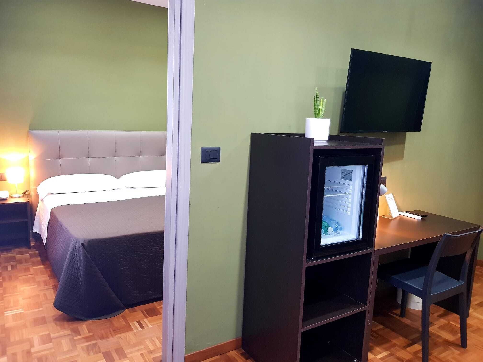 A hotel room with a bed, a desk with a chair, a television, and a small plant.