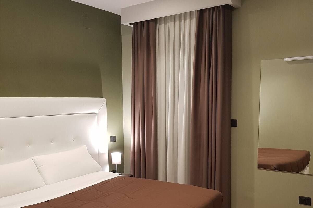 A modern bedroom with a large bed, a bedside table, a mirror, and a wooden floor.
