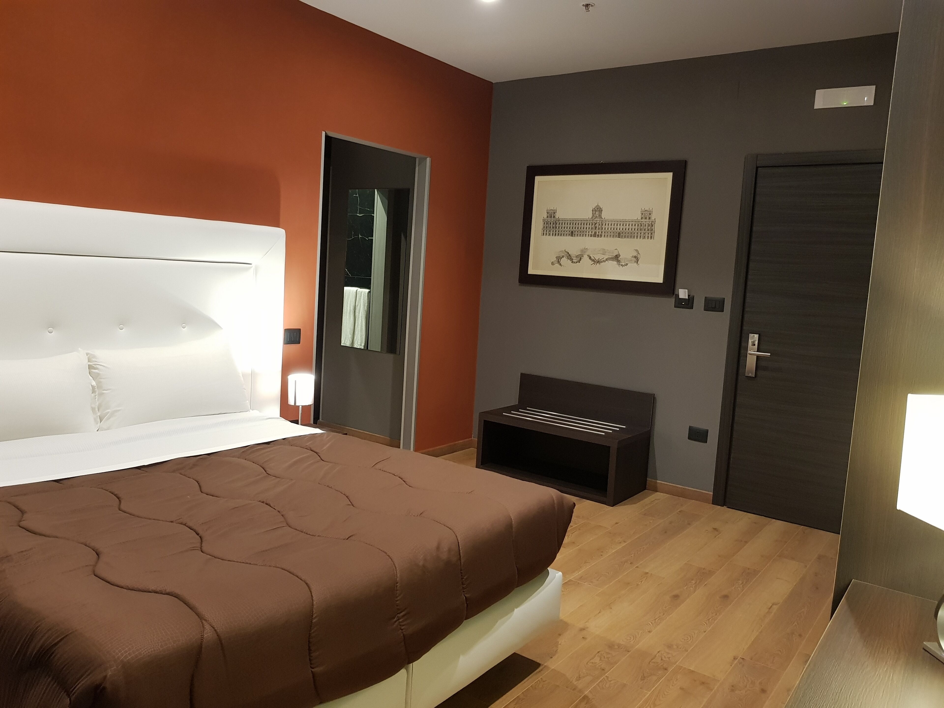 Una camera d'albergo moderna con un letto grande, un piccolo angolo salotto, un quadro appeso al muro e una porta.
