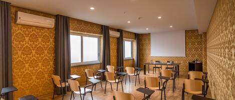 Un salón de conferencias con una pantalla de proyector, varias mesas y sillas dispuestas para reuniones.