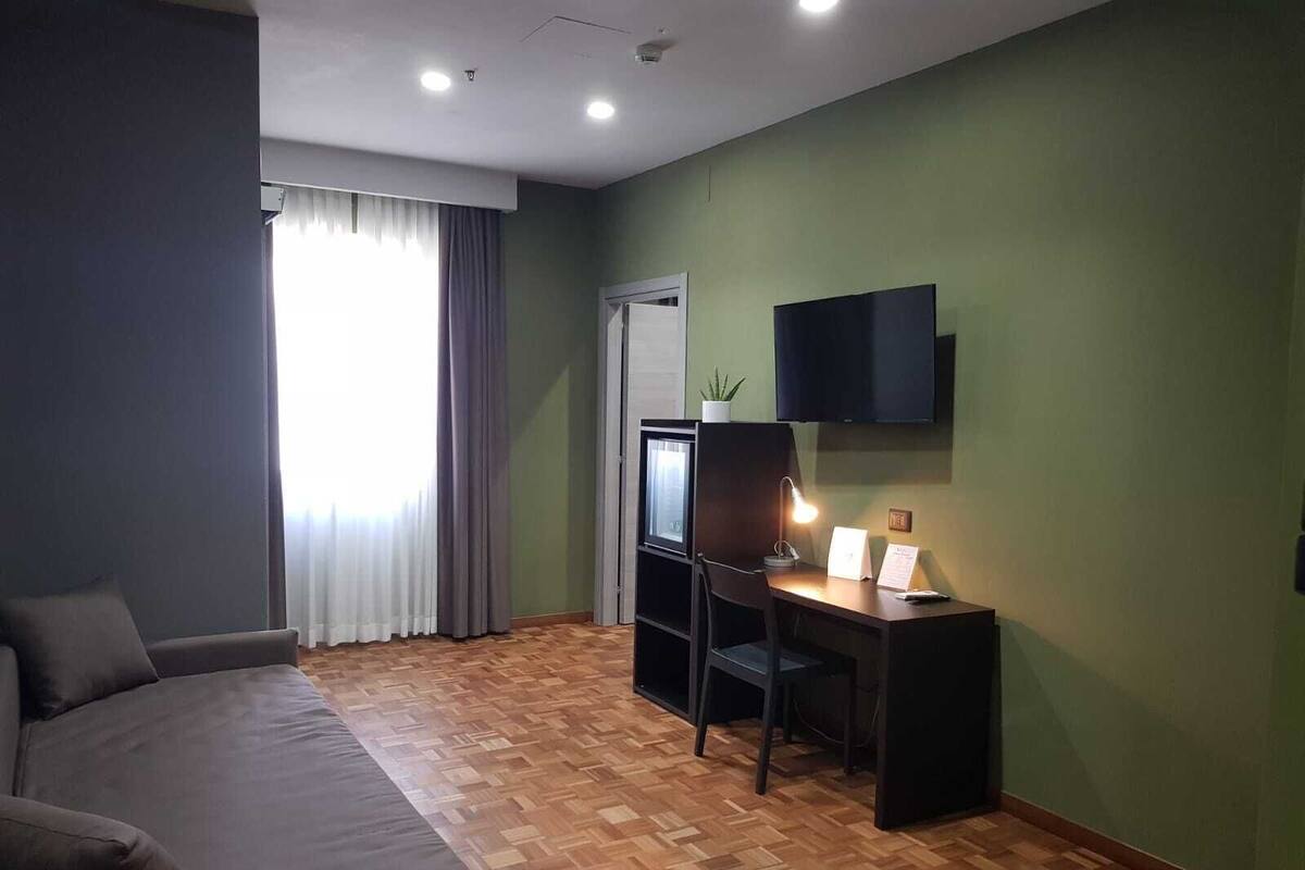 A modern room with a sofa, a desk with a computer, a TV, and a window with curtains.
