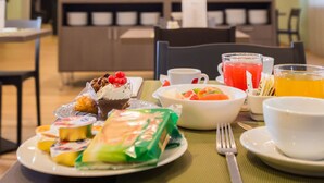 A breakfast setting with various food items and beverages on a table, including a dessert, fruit, and a juice.