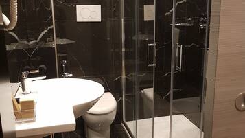 A modern bathroom with a glass-enclosed shower, a white sink, and a toilet.