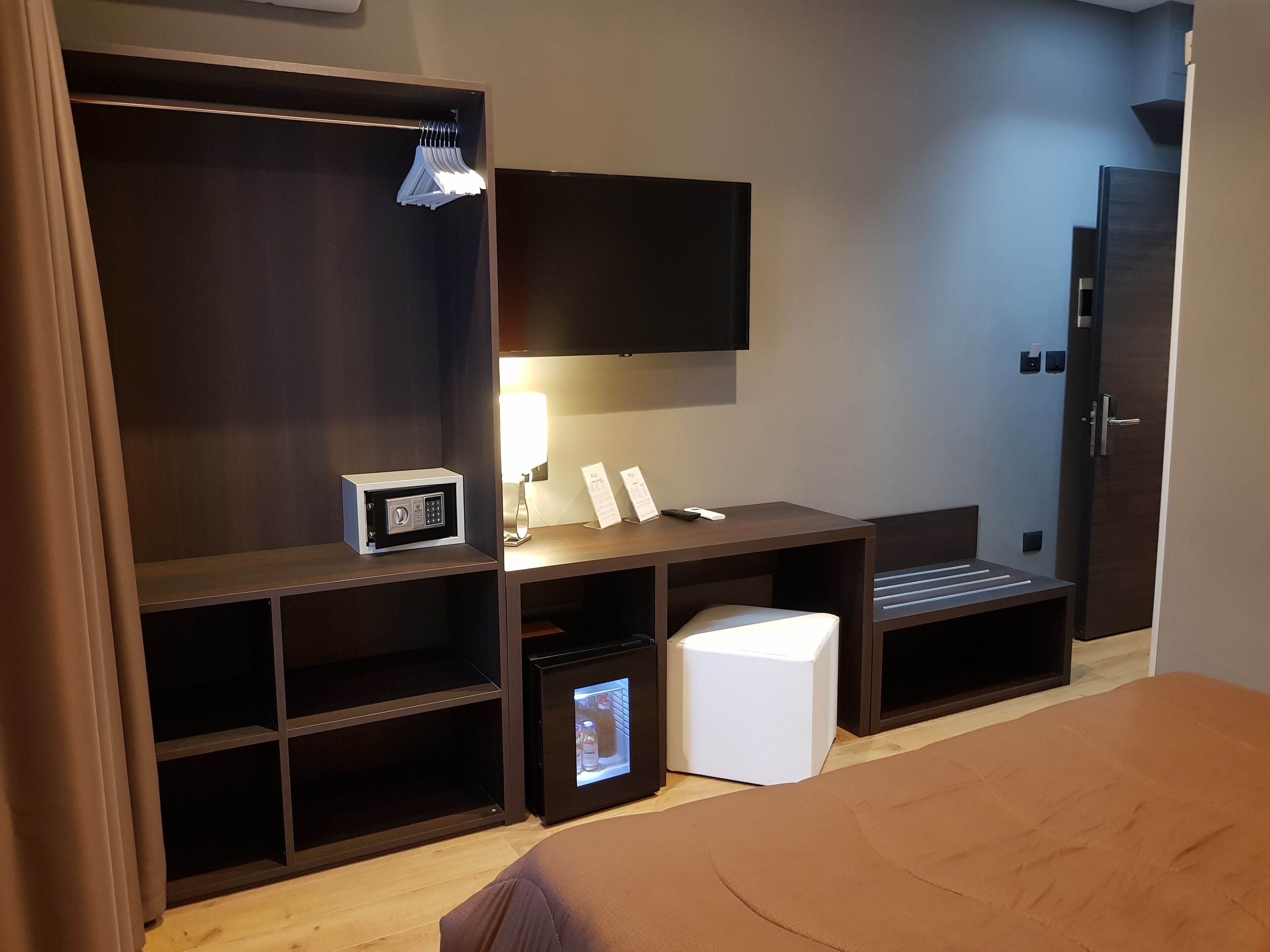 Una habitación de hotel con armario, escritorio con lámpara, refrigerador pequeño y cama.