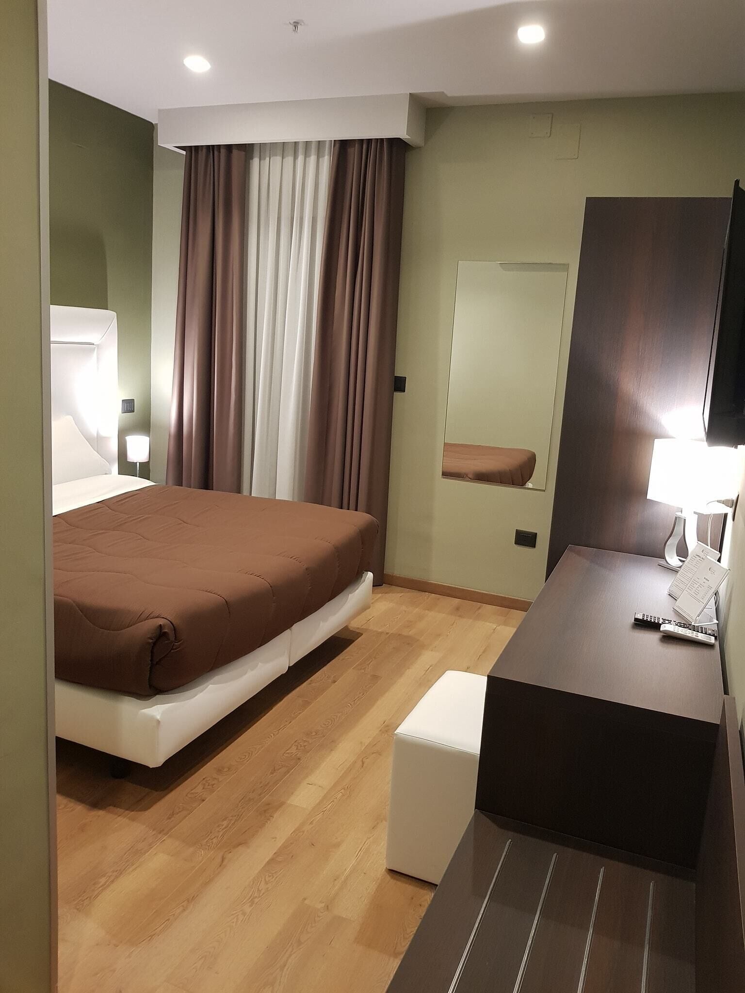 Habitación de hotel con cama, mesita de noche, espejo y un pequeño escritorio con una silla.