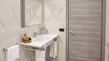 Un baño moderno con pared de mármol, un lavabo blanco, un bidé, un espejo grande y una puerta de madera.