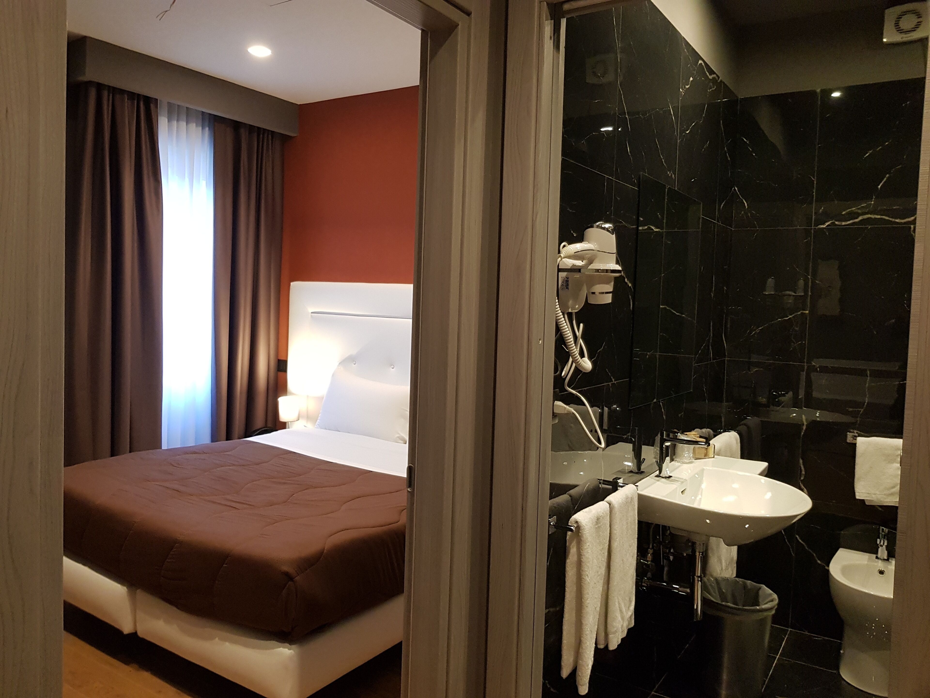 Ein Hotelzimmer mit Bett, Nachttischlampe sowie einem Badezimmer mit Waschbecken, Toilette und Bidet.