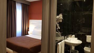 A hotel room with a bed, a bedside lamp, a bathroom with a sink, toilet, and bidet.