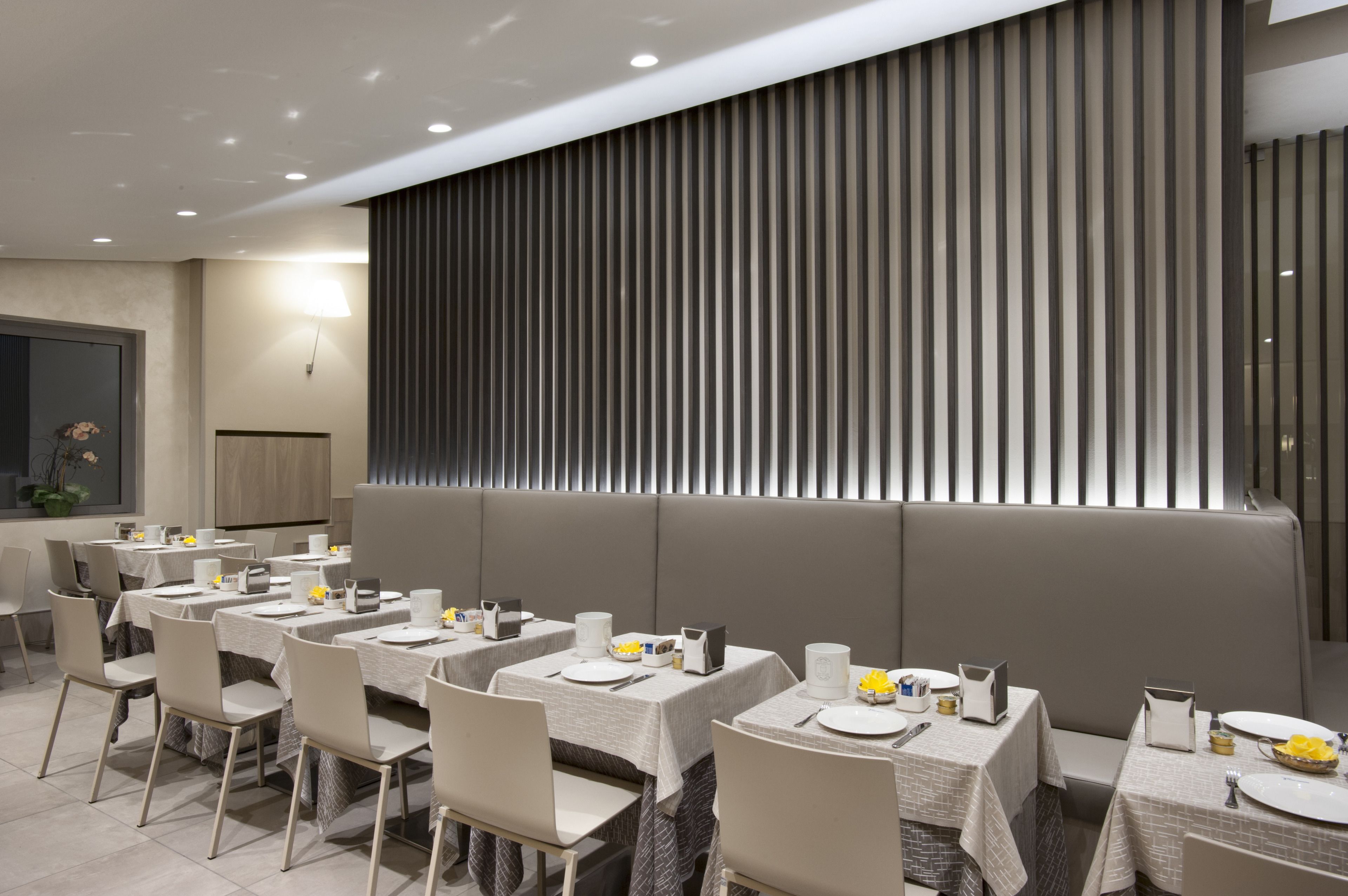 A modern dining area with multiple tables, each set with plates, cutlery, and a vase of yellow flowers.