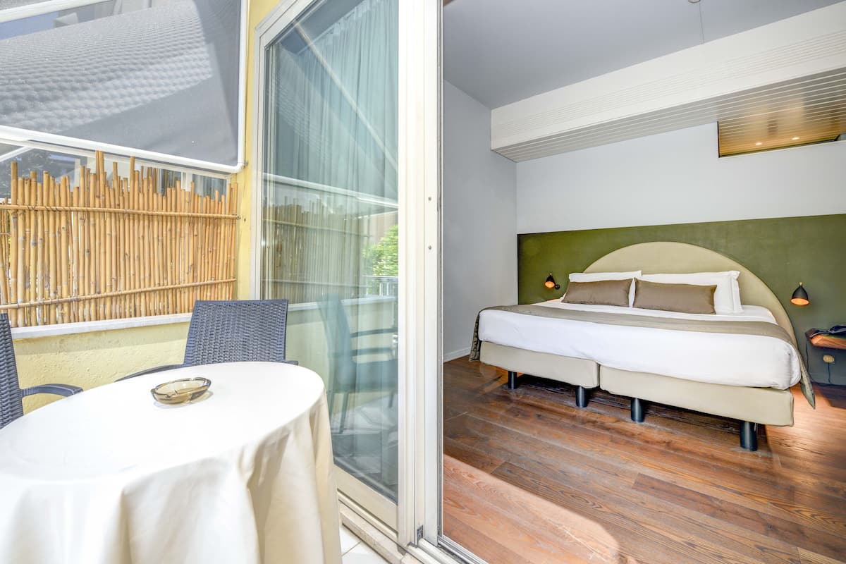 Een slaapkamer met een bed, nachtkastje en uitzicht op een bamboescherm door een glazen deur.