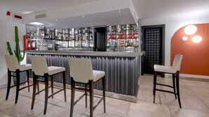 A bar area with a counter, multiple shelves of bottles, and four bar stools. - Hotel City (Desenzano del Garda)