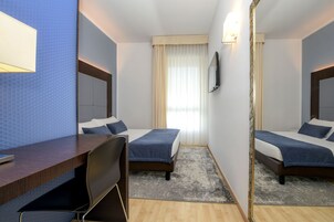Habitación de hotel con dos camas, un escritorio, una silla, un espejo y una ventana con cortinas.