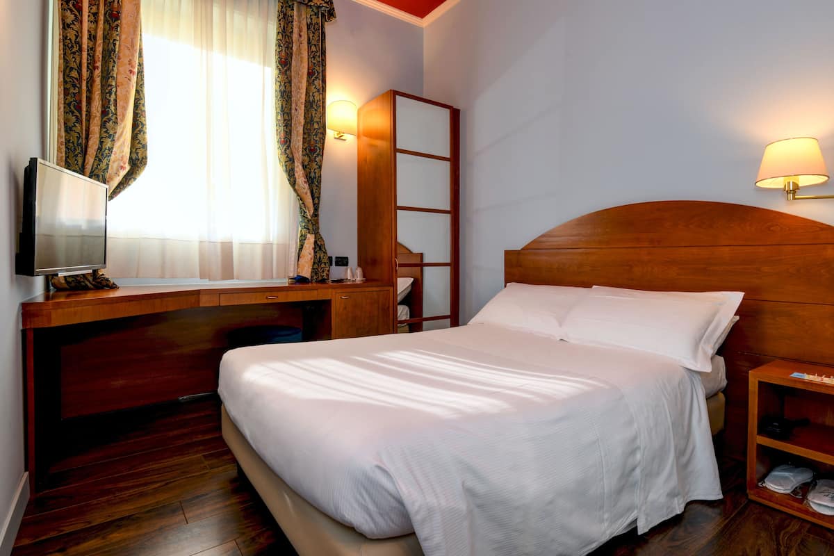 Een hotelkamer met een houten bed, een bureau met een televisie, een nachtkastje met een lamp en een grote spiegel.