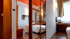 A hotel room with a wooden floor, a bed, a desk, a TV, and a window with curtains. - Hotel City (Desenzano del Garda)
