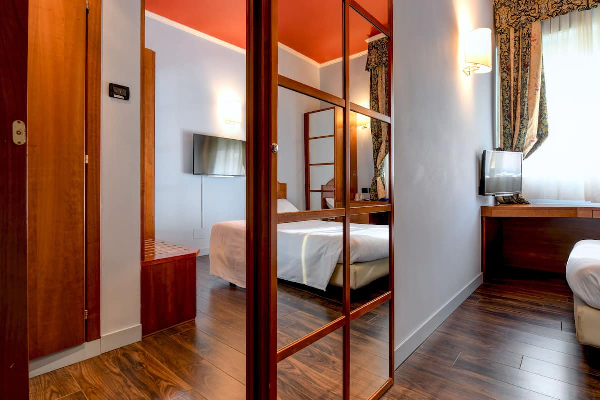 Een hotelkamer met houten vloer, een bed, een bureau, een televisie en een raam met gordijnen.