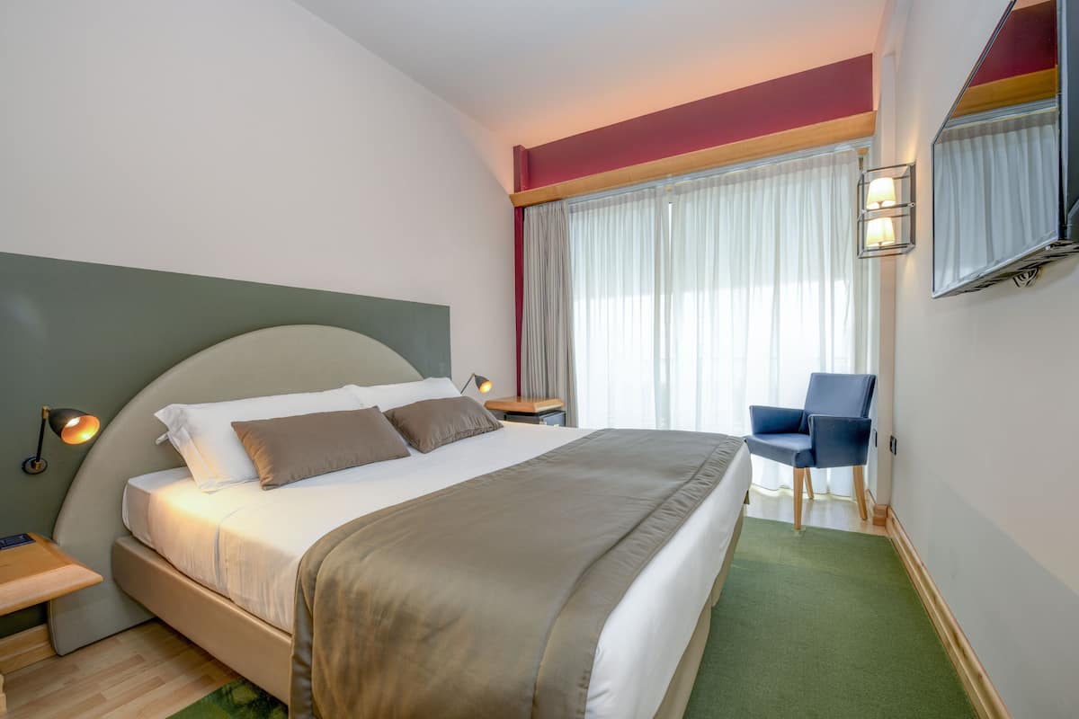 Een hotelkamer met een bed, een stoel, een televisie en een raam met gordijnen.