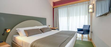 A hotel room with a bed, a chair, a TV, and a window with curtains.