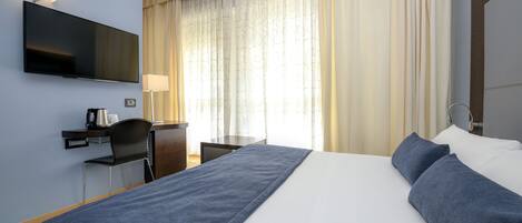 Una habitación de hotel con una cama grande, un escritorio con silla, un televisor de pantalla plana y una ventana con cortinas.