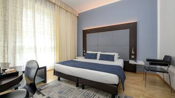 A modern hotel room with a large bed, a desk, and a chair.