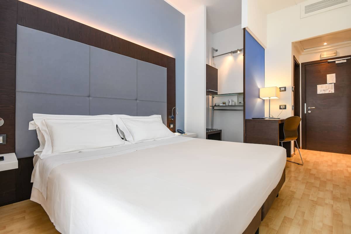 Een hotelkamer met een groot bed, een bureau, een stoel, een spiegel en een deur.