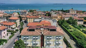 A hotel with a central courtyard, surrounded by buildings with red-tiled roofs, and a view of the sea and marina in the background.