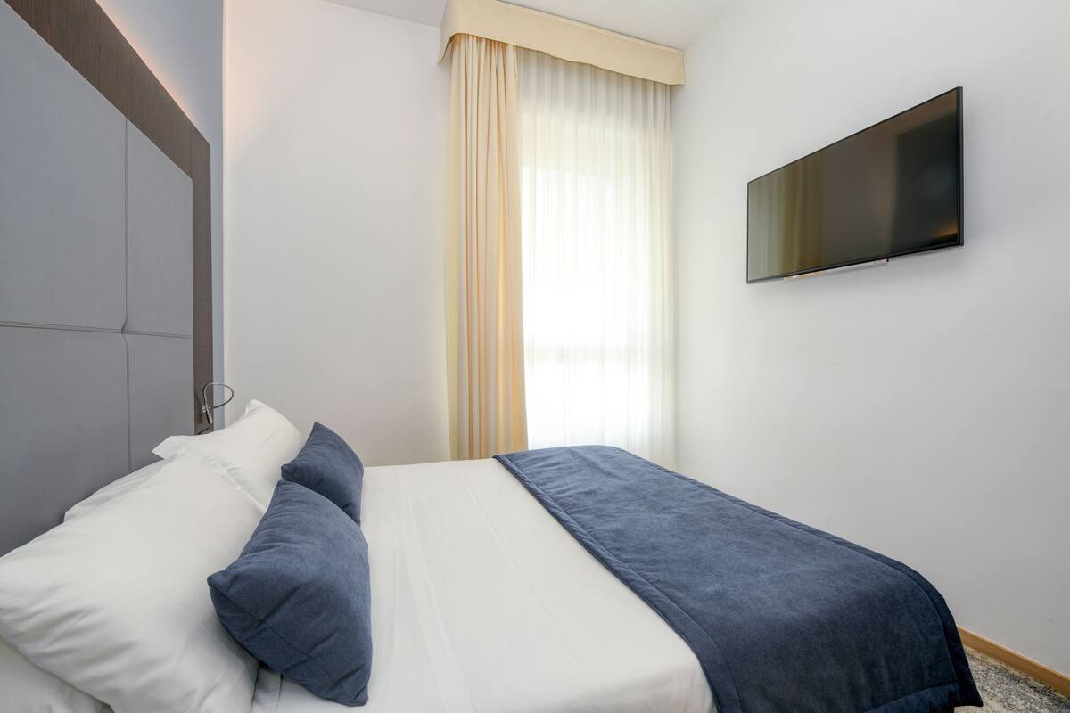 Een hotelkamer met een bed, een aan de muur bevestigde televisie en een raam met gordijnen.