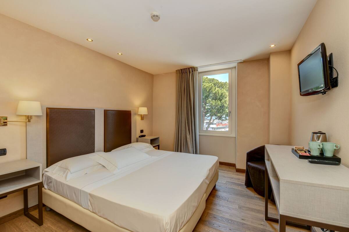 A hotel room with a bed, desk, chair, TV, and a window with curtains.