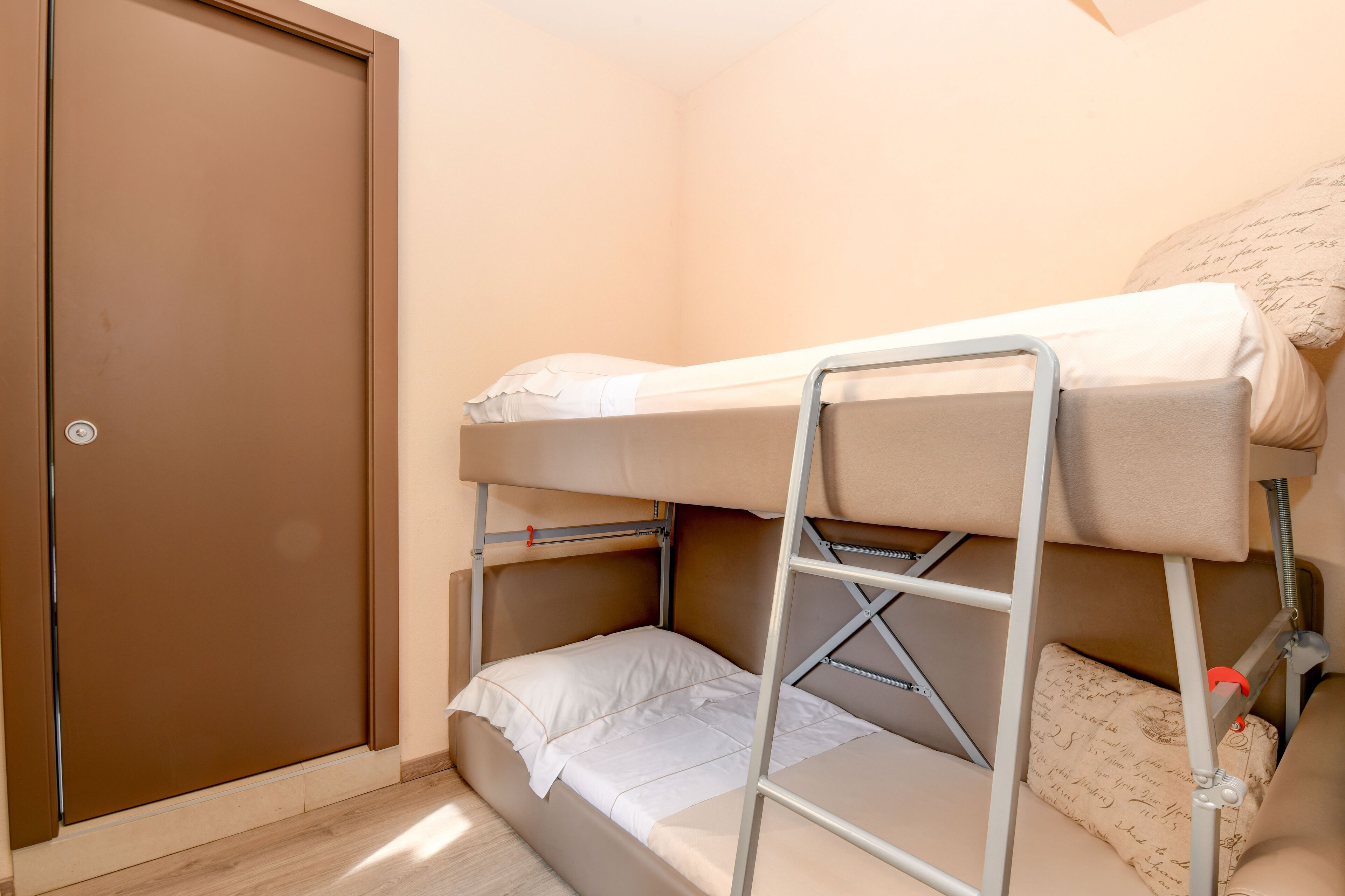 A bunk bed with a ladder, a door, and a small bedside table with a pillow.