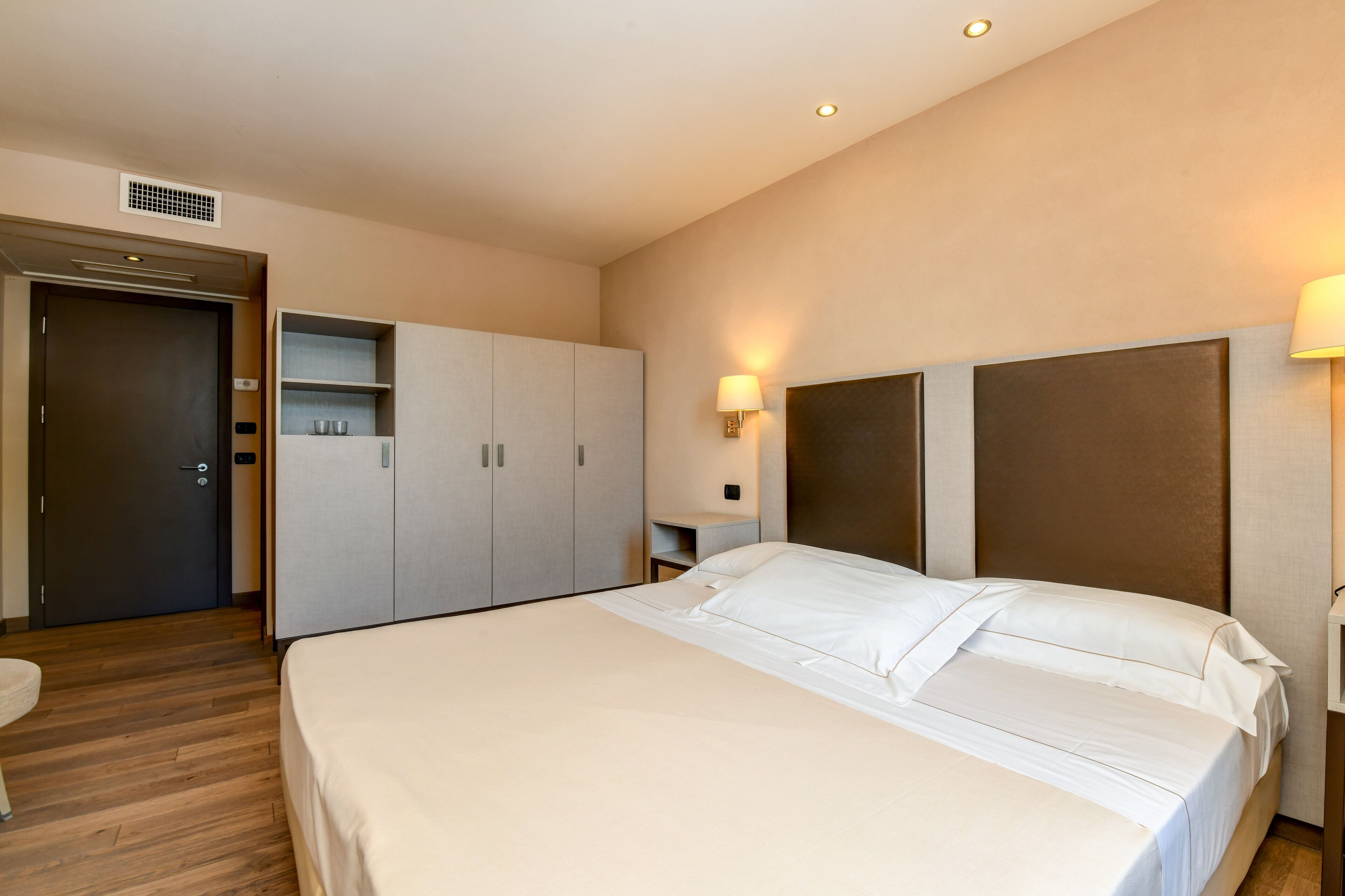 Una camera d'albergo con un letto, un armadio, un comodino e una lampada a parete.