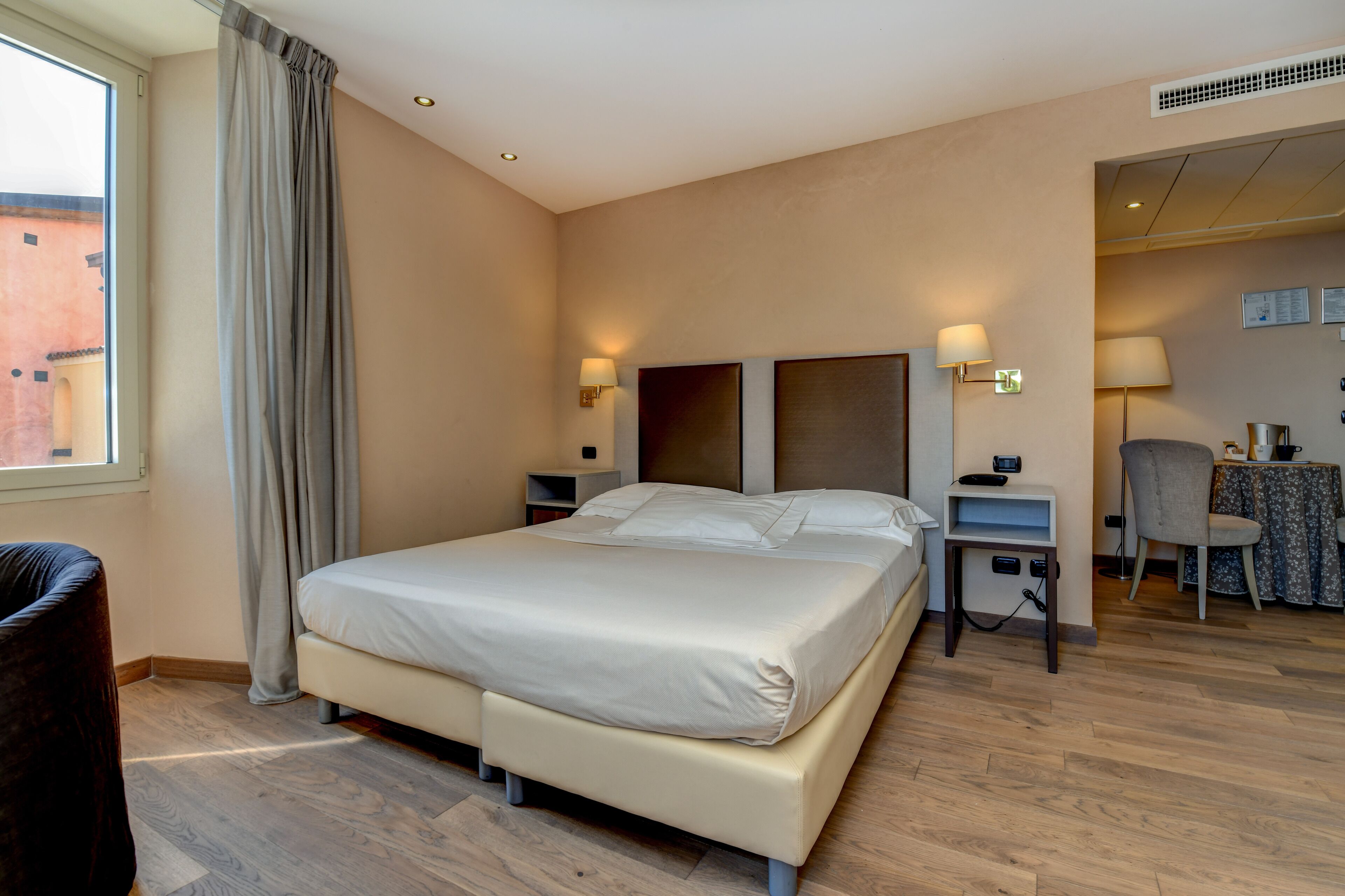 A hotel room with a large bed, bedside tables, a chair, and a desk with a lamp.