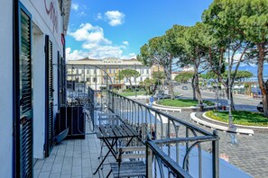 A balcony with a view of a street, a building with 'Splendid Mayer' sign, and a roundabout with trees. - Hotel Tripoli (Desenzano del Garda)