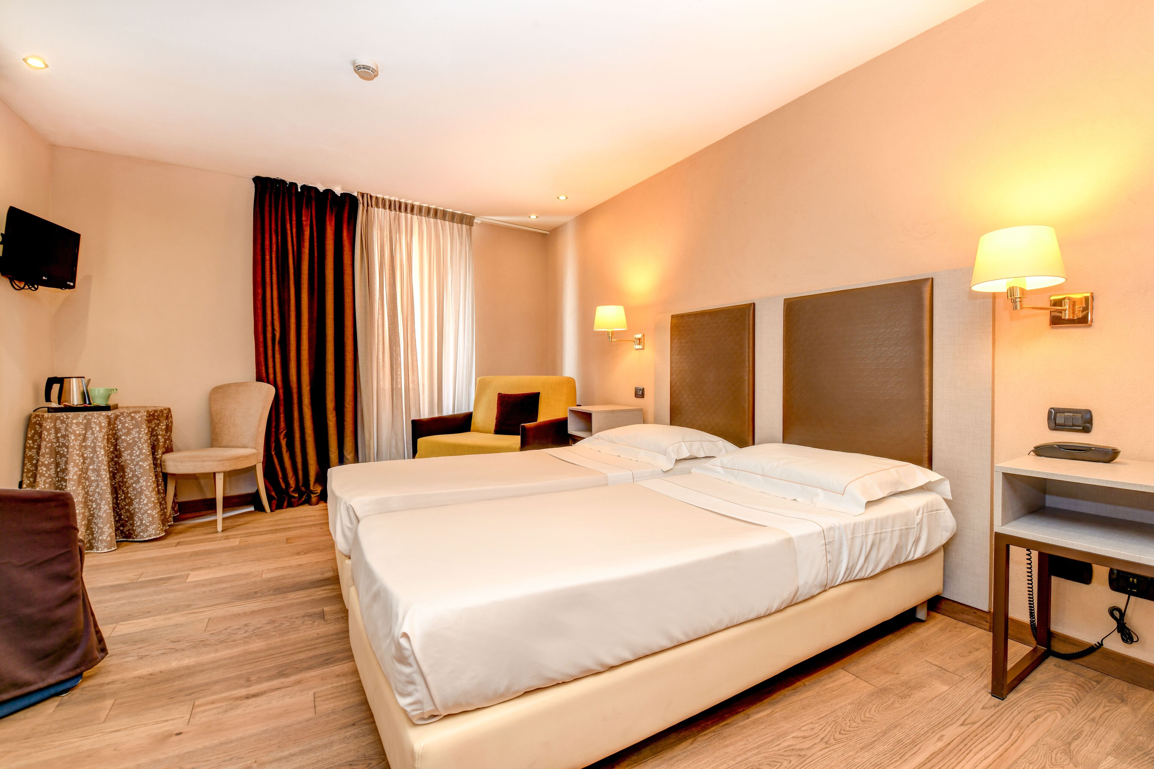 Quarto de hotel com uma cama grande, uma escrivaninha, uma cadeira, uma televisão e um abajur.